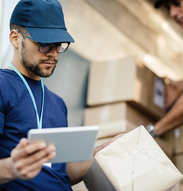 young-delivery-man-using-touchpad-while-reading-label-package (1)